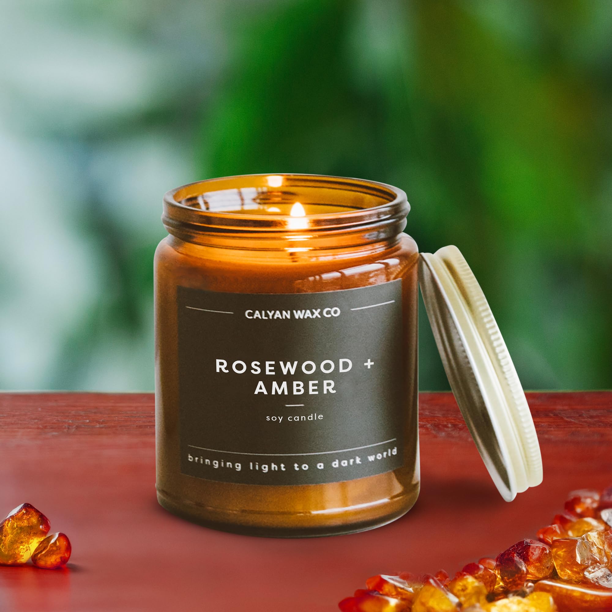 Calyan Wax Co. Rosewood & Amber: bougie allumée dans un verre ambré.